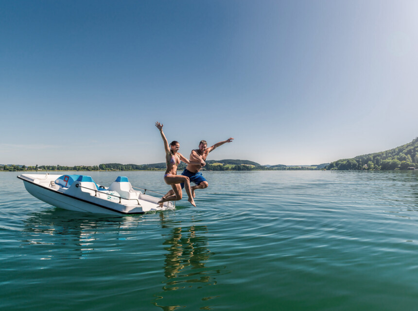 Ein Paar springt vom Boot aus in den See