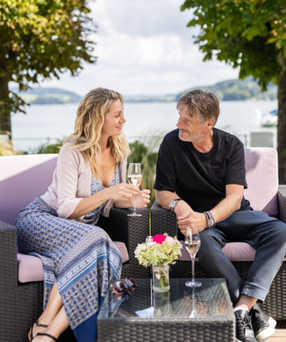 Beim Romantik-Kurzurlaub in Österreich genießt ein Paar ein Glas Sekt auf der See-Terrasse