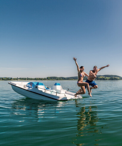 Ein Paar spring beim Romantikurlaub am See in Österreich von einem Boot ins Wasser