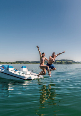 Ein Paar springt beim Pärchenurlaub in Österreich vom Boot in den See