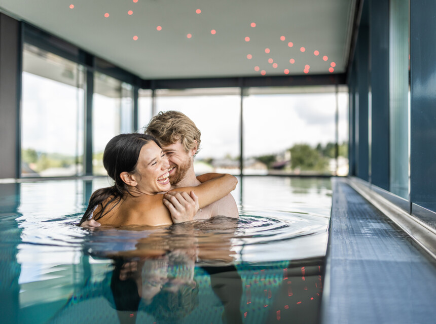 Im Kuschelhotel bei Salzburg umarmt sich ein Paar im Panorama-Pool