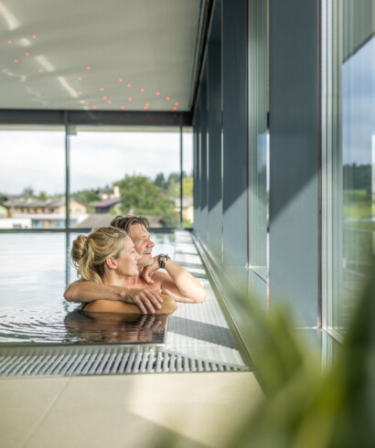 Ein Paar genießt im Wellnesswochenende bei Salzburg den Seeblick vom Pool aus 