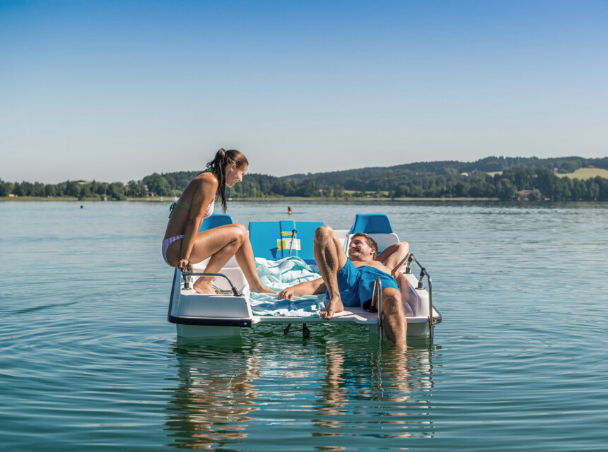 Ein junges Pärchen genießt im Sommerurlaub am Mattsee die gemeinsame Zeit auf einem Tretboot und lässt sich sonnen.