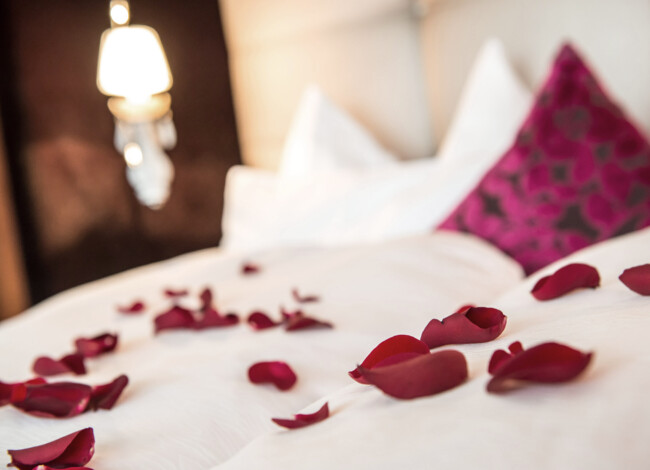 Rote Rosenblüten liegen auf einem weiß bezogenen Bett